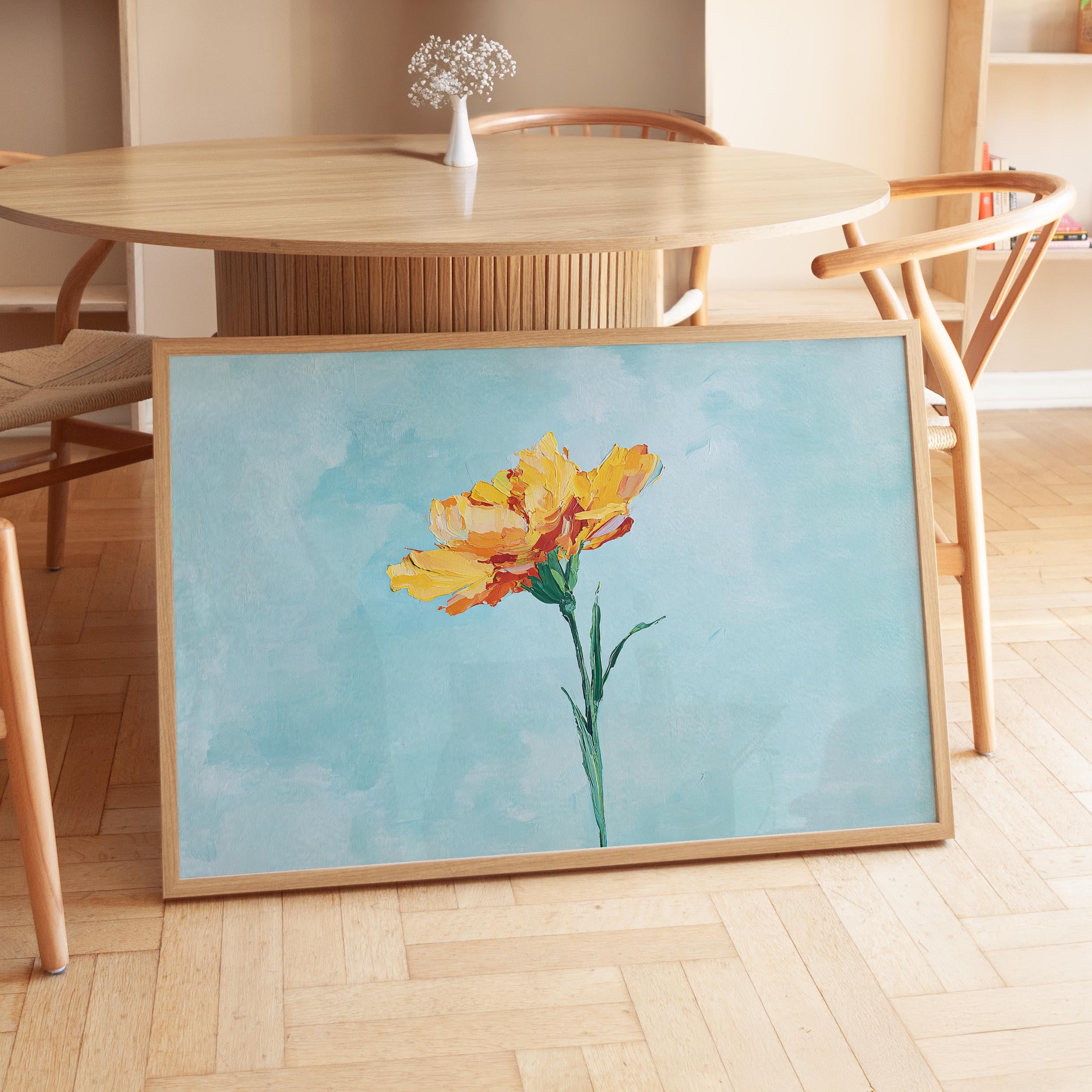 a large framed painting of a yellow flower on a wooden table.