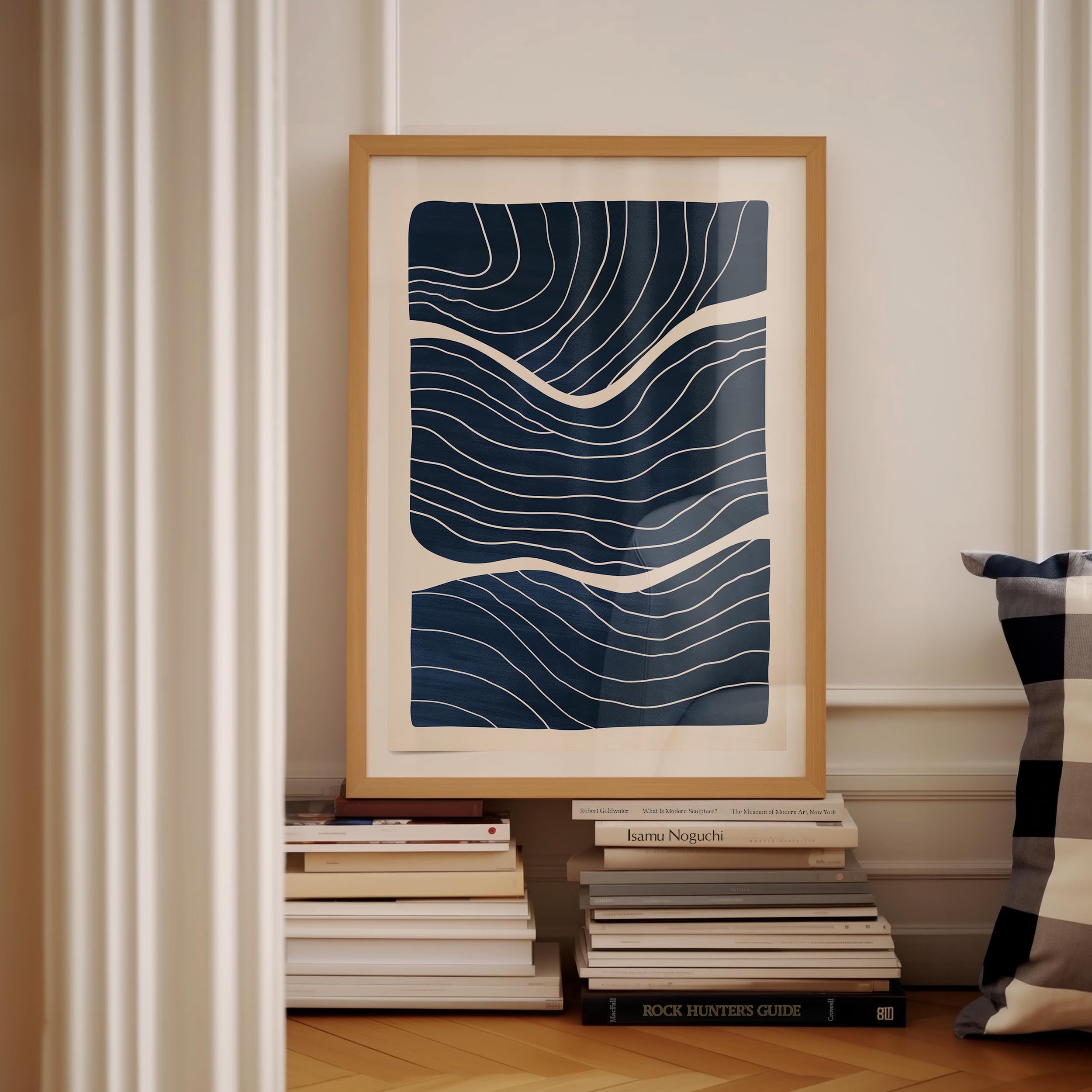 a framed abstract art piece with a blue and white color scheme, displayed on a white wall next to a stack of books.