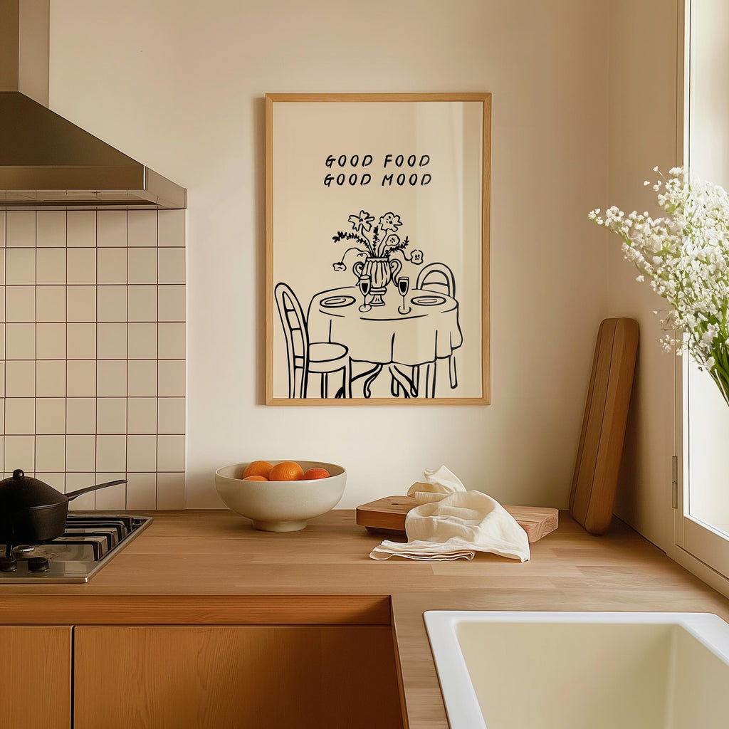 a kitchen counter with a bowl of fruit, a vase of flowers, and a framed poster with a table and chairs.