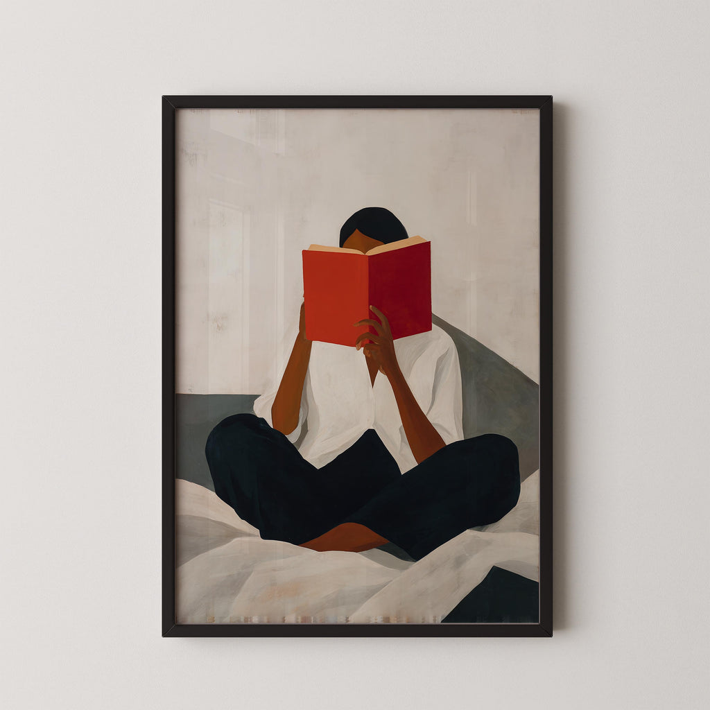 A person is sitting cross-legged on a bed, reading a red book.