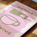 A pink and white poster with the word "MATCHA" written on it, along with a stylized illustration of a cup and a whisk.