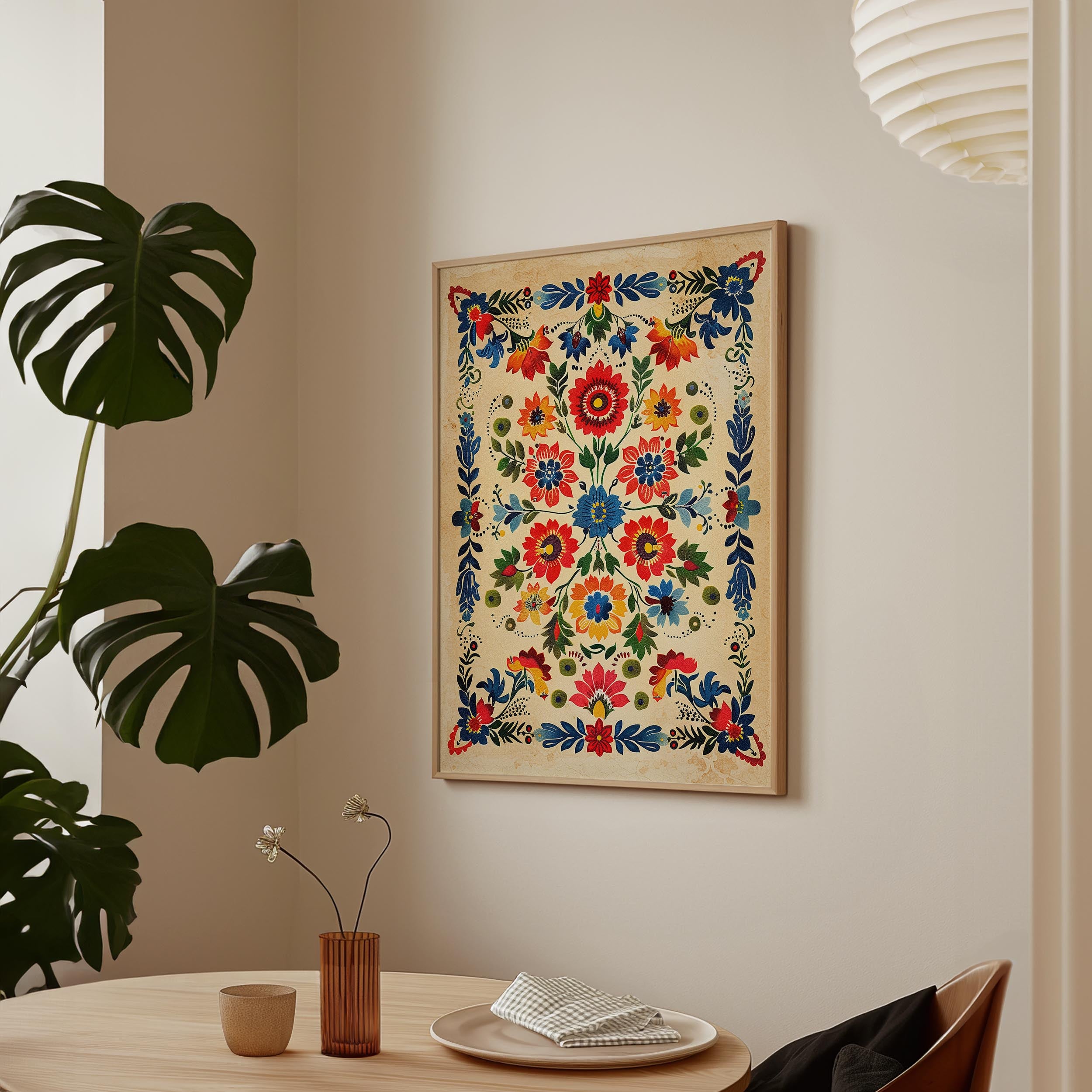 a wooden table with a vase of flowers, a plate, and a cup, set against a wall with a framed picture of a colorful floral design hanging above it.