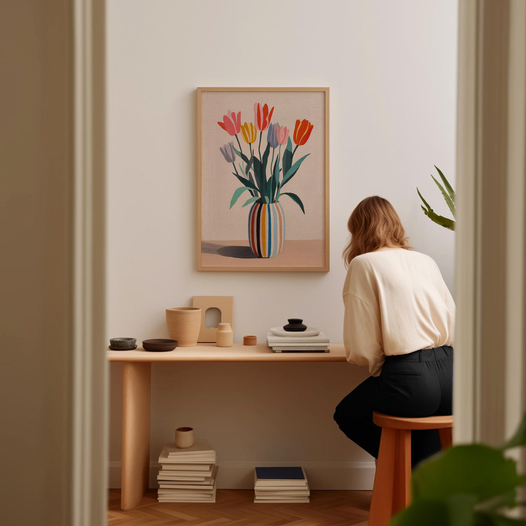 A woman is sitting at a wooden desk, surrounded by various objects, including a vase with colorful flowers, books, and a plant.