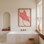 a modern bathroom with a large white bathtub, a framed artwork of a red and white striped swimsuit, and a window with a vase of flowers.