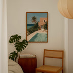 a painting of a tropical beach scene with a pool and palm trees, hanging on a wall above a wooden chair and a small table.