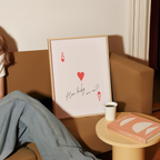 a person sitting on a couch with a framed print of a red heart and the text "How lucky are we?" next to a small table with a book and a cup of coffee.