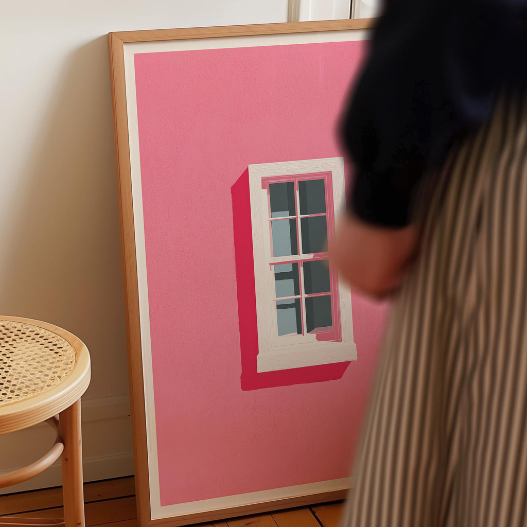 a person standing next to a large framed artwork depicting a pink building with a white window.