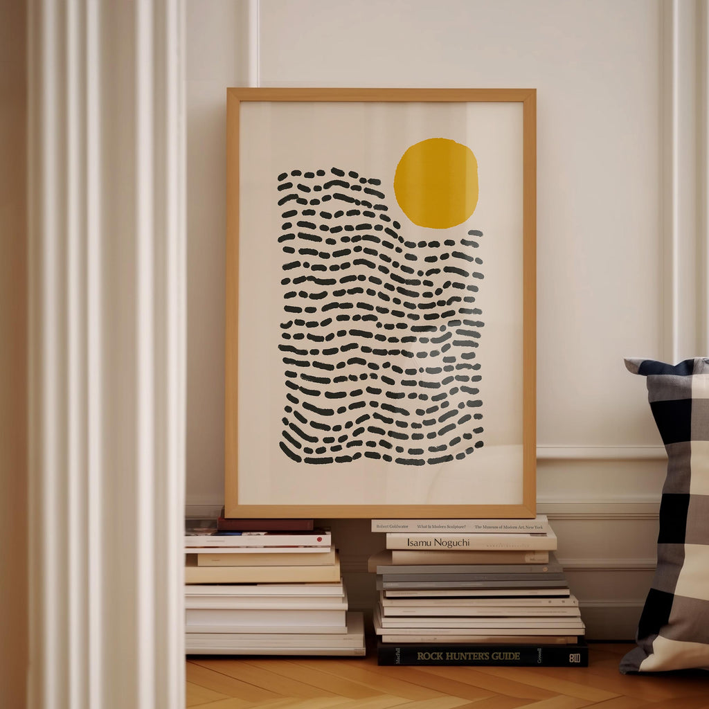 a framed abstract art print with a black and white striped pattern, hanging on a wall next to a stack of books.