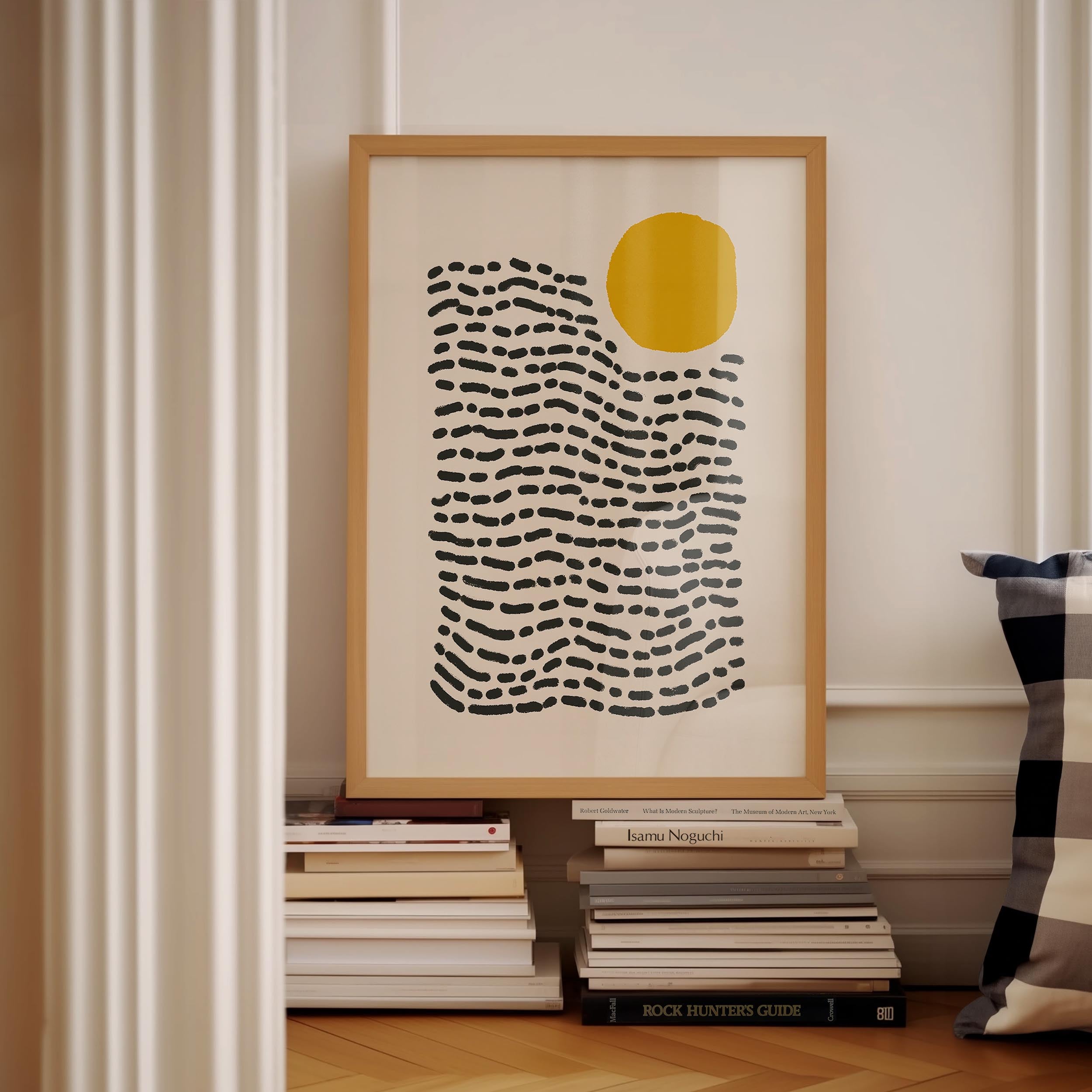 a framed abstract art print with a black and white striped pattern, hanging on a wall next to a stack of books.