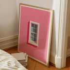 a large pink poster of a window on a wall, leaning against a white wall.