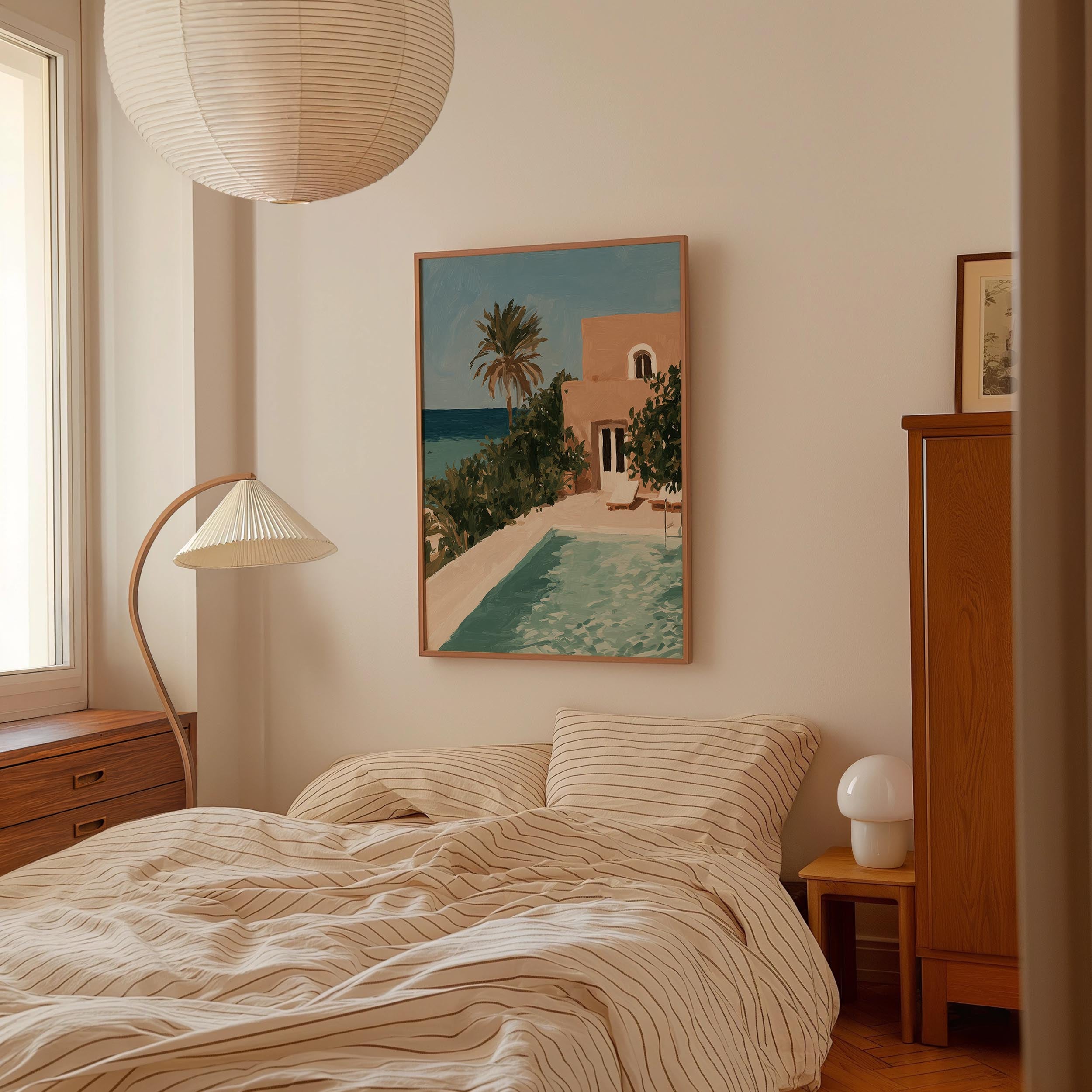 a bedroom with a bed, a lamp, and a painting of a pool and palm trees on the wall.