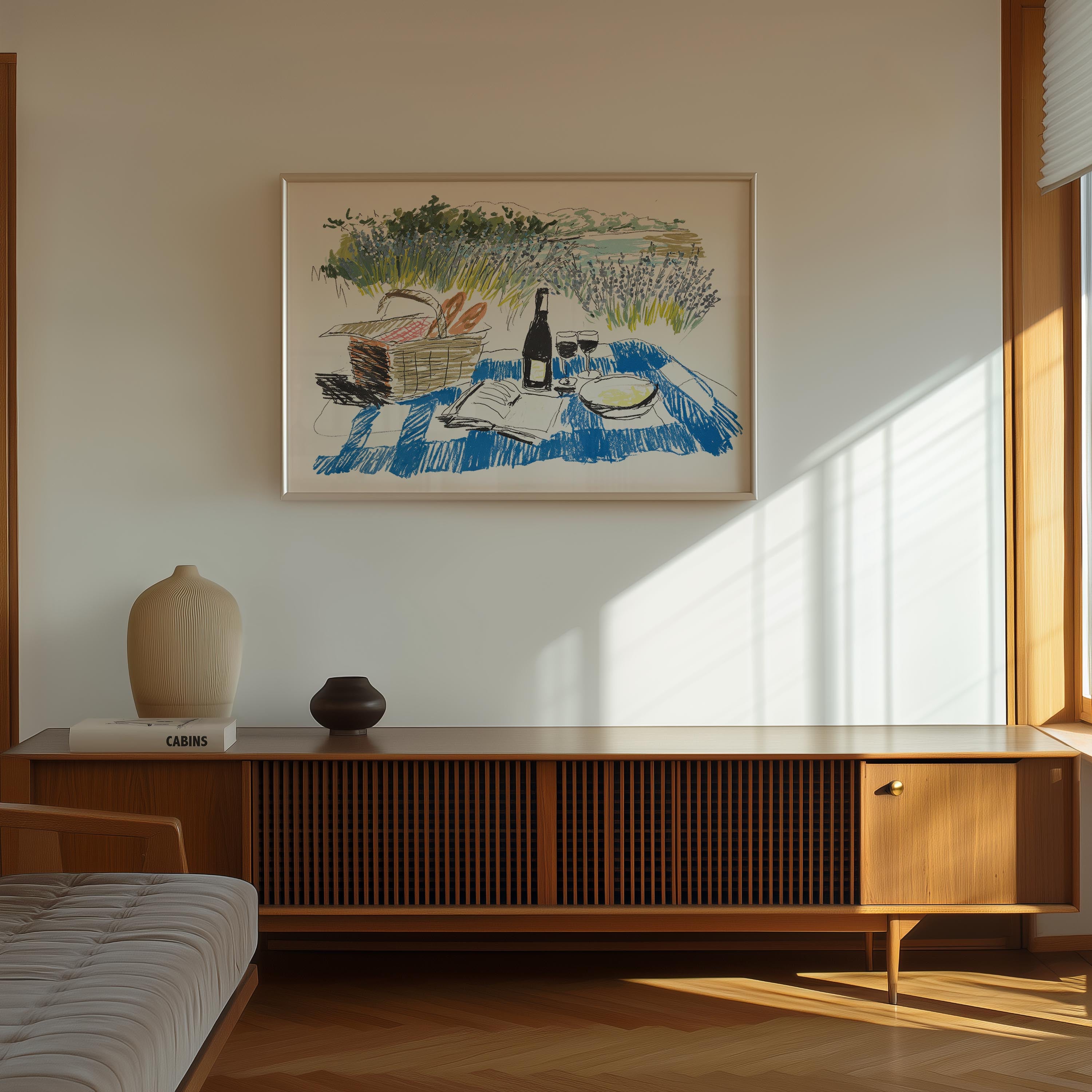 a wooden cabinet with a vase and a book on top, and a framed painting of a picnic scene hanging on the wall above it.