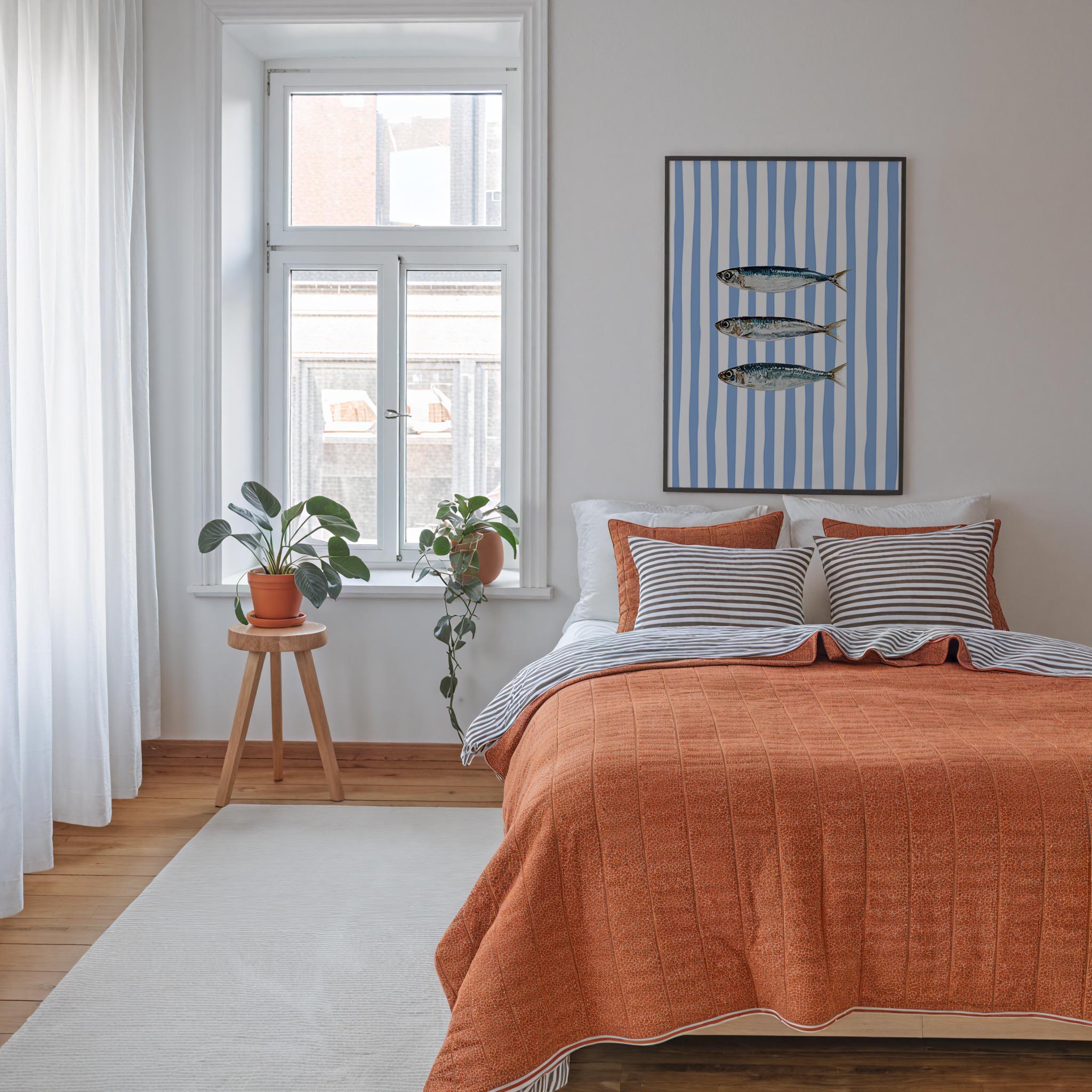 a cozy bedroom with a large bed, a window with a plant on the sill, and a framed artwork featuring fish on the wall.