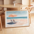 A framed painting depicting a beach scene with a beach umbrella, lounge chairs, and the ocean in the background.