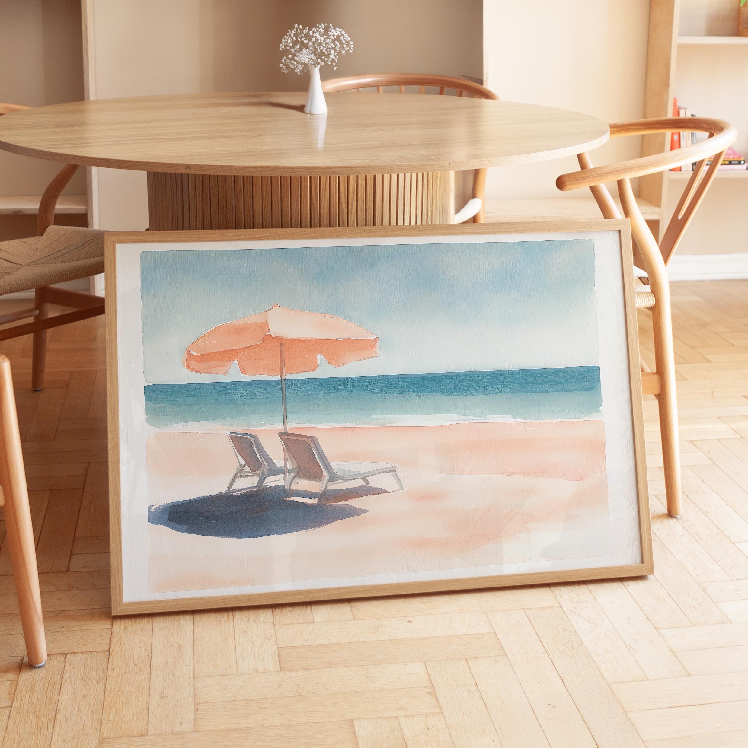 A framed painting depicting a beach scene with a beach umbrella, lounge chairs, and the ocean in the background.