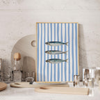 a framed artwork of three fish on a blue and white striped background, placed on a shelf or table.